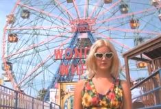 a woman wearing sunglasses standing in front of a ferris wheel