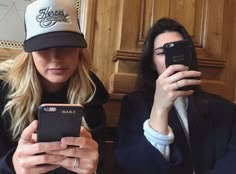 two women sitting next to each other while looking at their cell phones in front of them