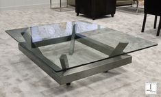 a glass and metal coffee table on carpeted floor with chairs in the back ground