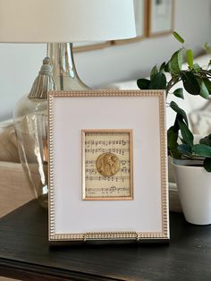 a table with a lamp, potted plant and framed music sheet art on it