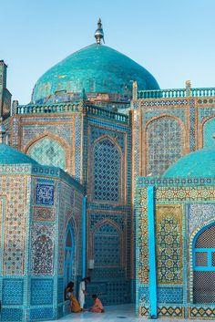 two women sitting on the ground in front of a building with blue and green tiles