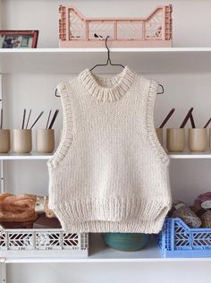 a white sweater hanging on a shelf next to yarn and crocheted items in baskets