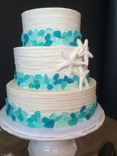 a three tiered cake with blue and white frosting on a table next to utensils