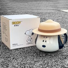 a coffee mug with a hat on it sitting next to a box that says snoopy