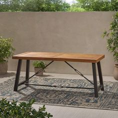 a wooden table sitting on top of a rug in front of a wall and potted plants