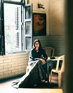 a woman sitting in a chair next to a table with a painting on the wall