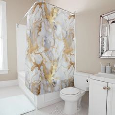 a white toilet sitting next to a bath tub in a bathroom under a mirror with gold paint on it