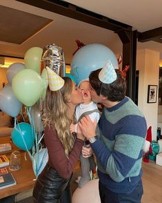 a man kissing a woman while holding a baby in front of balloons and streamers