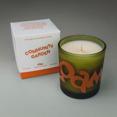 a green candle sitting next to a box on a gray surface with the words community garden printed on it