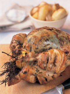 a cooked chicken on a cutting board with potatoes in the background