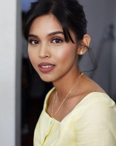 a close up of a person wearing a yellow shirt and gold necklace on her neck