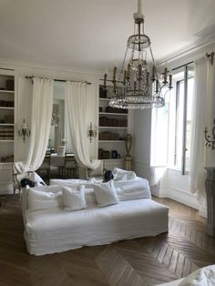 a living room filled with white furniture and a chandelier hanging from the ceiling