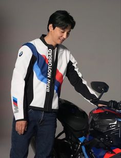 a man standing next to a motorcycle with his hand on the handlebars and wearing a colorful jacket