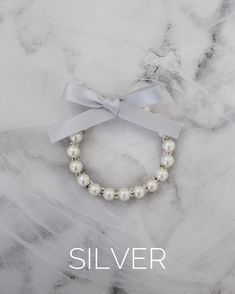 a bracelet with pearls and a bow on it that says silver, in front of a marble background