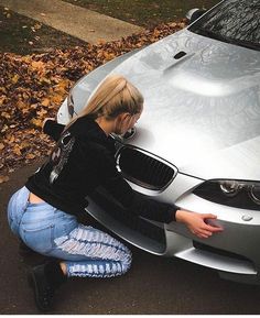 a woman kneeling down next to a silver car