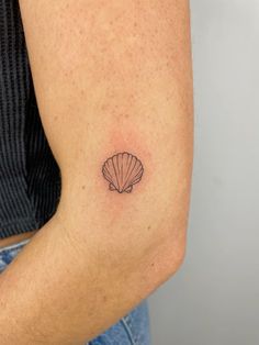 a woman's arm with a small shell tattoo on it