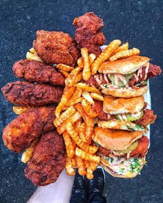 a person is holding a plate full of fried chicken and french fries on the street