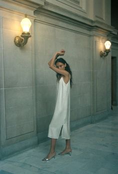 a woman standing in front of a wall with her arm up and arms behind her head