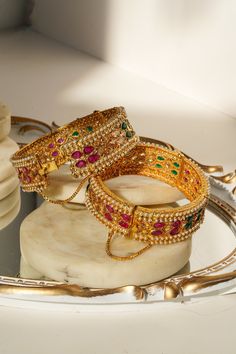 Introducing the Amika Bangle Set (Set of 2), a stunning addition to any jewelry collection. These gold-plated bangles feature intricate designs adorned with pearls and vibrant multicolor stones, including green and ruby accents. The detailed floral and petal patterns exude elegance and sophistication, making these bangles & bracelets set perfect for desi weddings and special occasions. The Amika Bangle Set showcases the timeless beauty of Navratan craftsmanship. The bangles are designed with an Navratan Bangles, Bangles And Bracelets, Bangles Set, Gold Plated Bangles, Bangle Bracelet Set, Bracelets Set, Bangles Bracelets, Desi Wedding, Le Lot