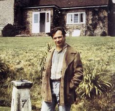 a man standing in front of a house next to a stone pillar and planter