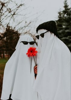 two people dressed in white and black holding a red flower