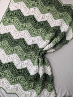 a green and white crocheted blanket laying on top of a bed next to a pillow