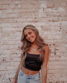 a woman standing in front of a brick wall with her hand on her hip and smiling