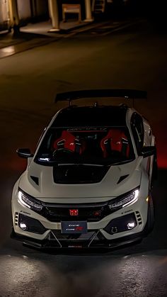 the front end of a white car with its hood open at night in a parking lot