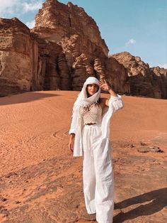 a woman standing in the desert with her hands on her head and wearing a white outfit