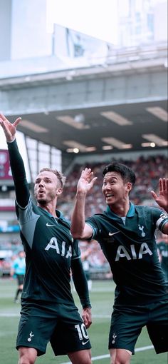 two men are playing soccer in front of an audience at a stadium with their hands up