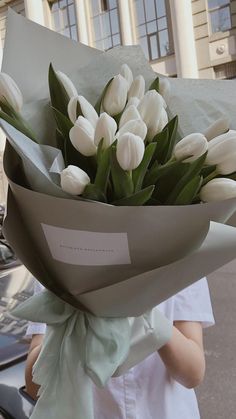 a woman holding a bouquet of white tulips in front of a building on the street