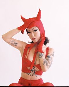 a woman in a red outfit with horns on her head and hands behind her head