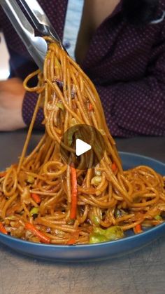 someone using tongs to stir noodles on a plate