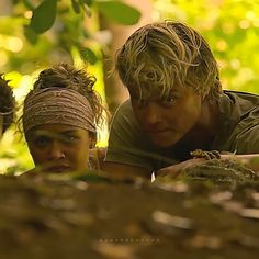 two men and a woman in the jungle looking at something on the ground with trees behind them