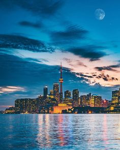 the city skyline is lit up at night as seen from across the water in front of a full moon