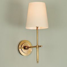 a wall light with a white shade on the side and a gold metal pole attached to it