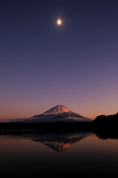 a full moon is seen over a mountain in the distance with water reflecting it's surface