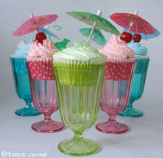 three cupcakes with umbrellas and cherries on top in glass vases