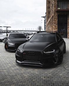 two black cars parked next to each other on a brick road