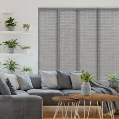 a living room with grey couches and plants on the wall