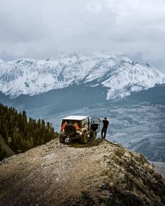 two men standing on top of a mountain next to a car