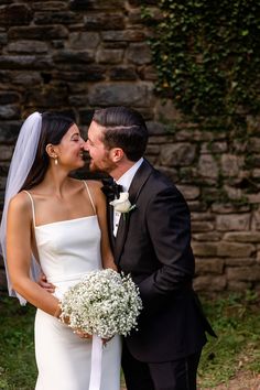 a newly married couple kissing each other in front of a stone wall and greenery