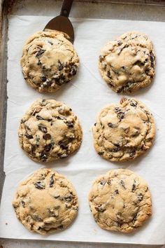 six chocolate chip cookies sitting on top of a baking sheet next to a spatula