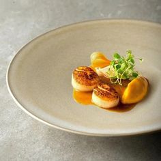 two scallops on a plate with sauce and garnish