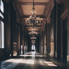 an empty hallway with chandeliers and windows in the center is lit by sunlight