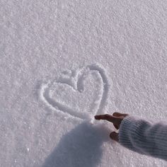 a person is holding their hand out to draw a heart in the snow