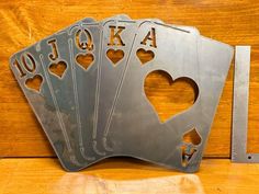 four metal playing cards with the letters oka and hearts cut out of them on a wooden table