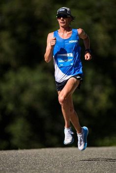 a man running in a marathon wearing a blue shirt and black hat with trees in the background