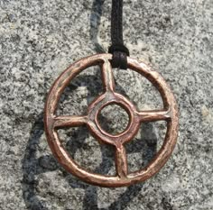 a metal pendant with a circular design on a black leather cord hanging from a rock