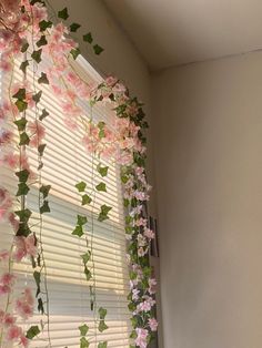 pink flowers hanging from the side of a window sill in front of a blinds